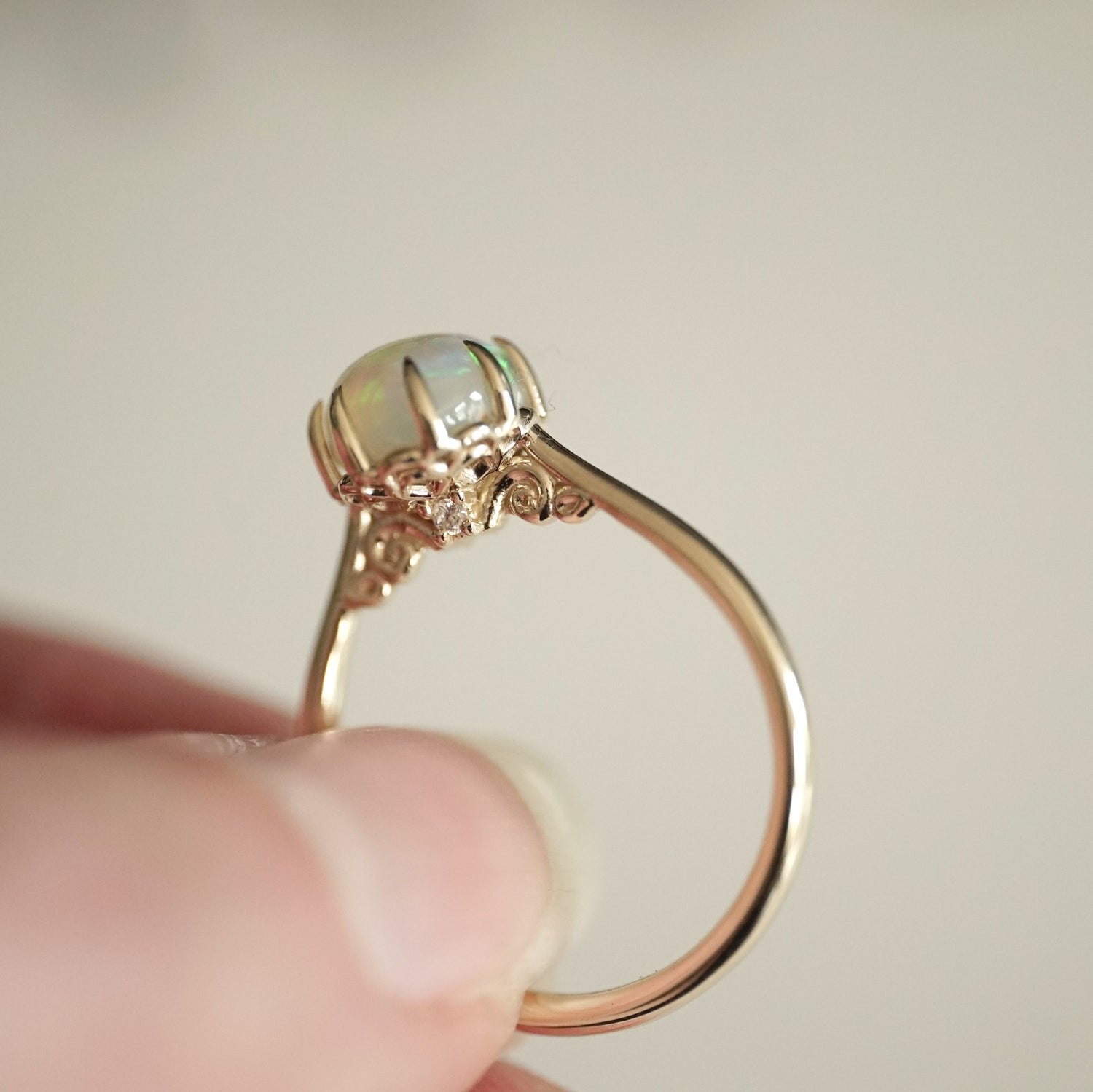 a yellow gold ring with an opal center stone turned to display the underside basket detail with a single round diamond accent in a light skinned hand
