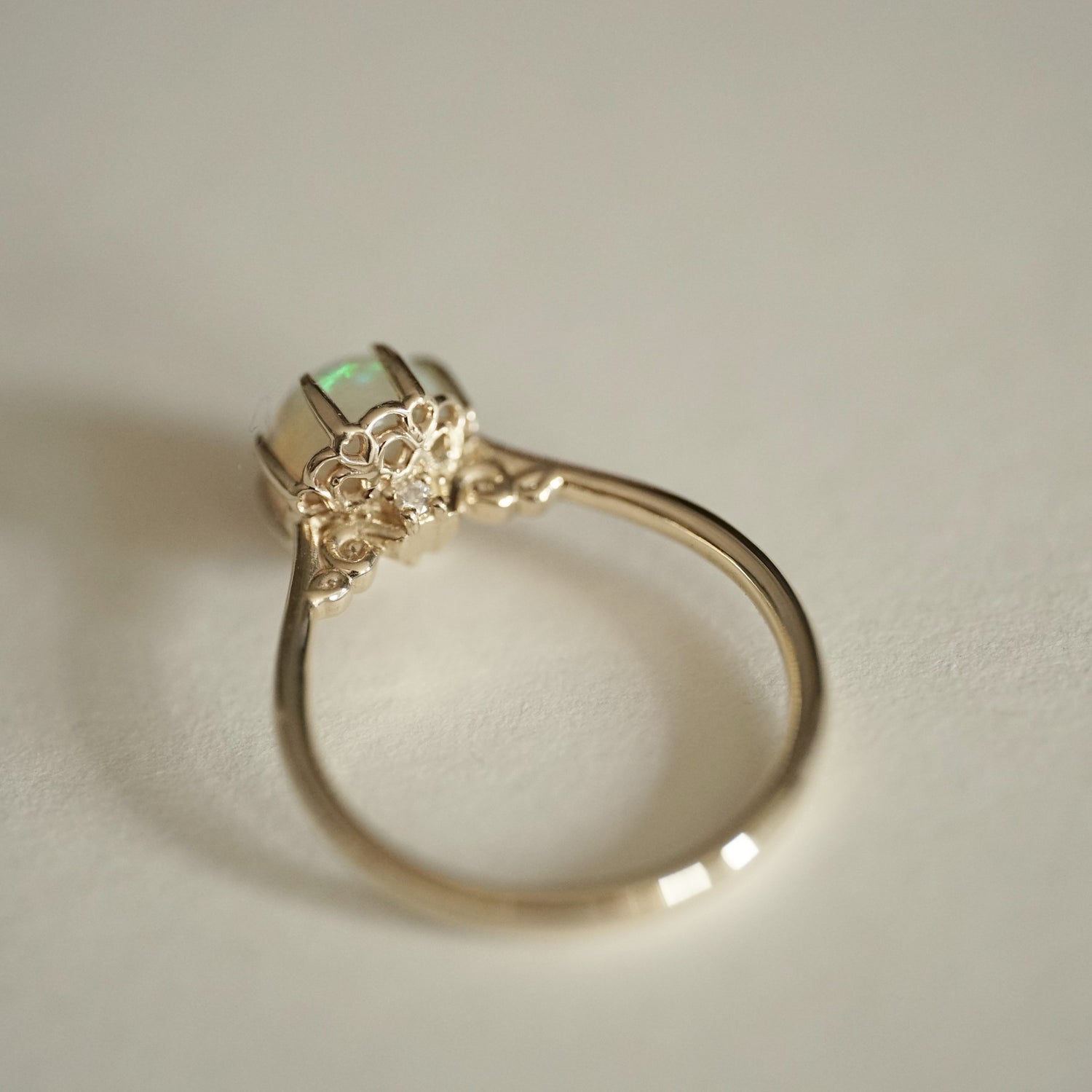 a yellow gold ring with an opal center stone turned to display the underside basket detail with a single round diamond accent