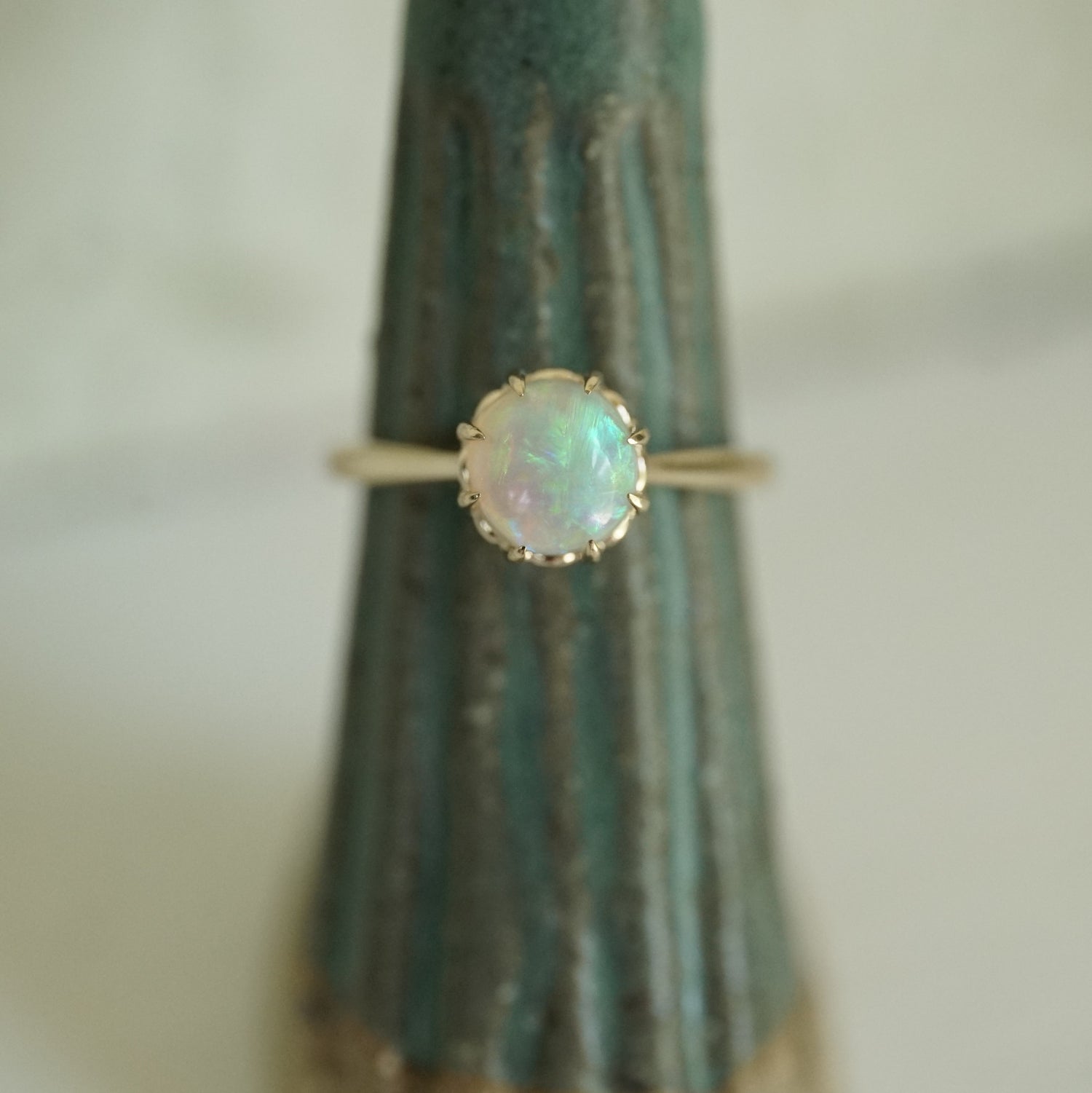 a vibrant opal with brushstroke patterns in an 8 prong yellow gold setting on a green ceramic display