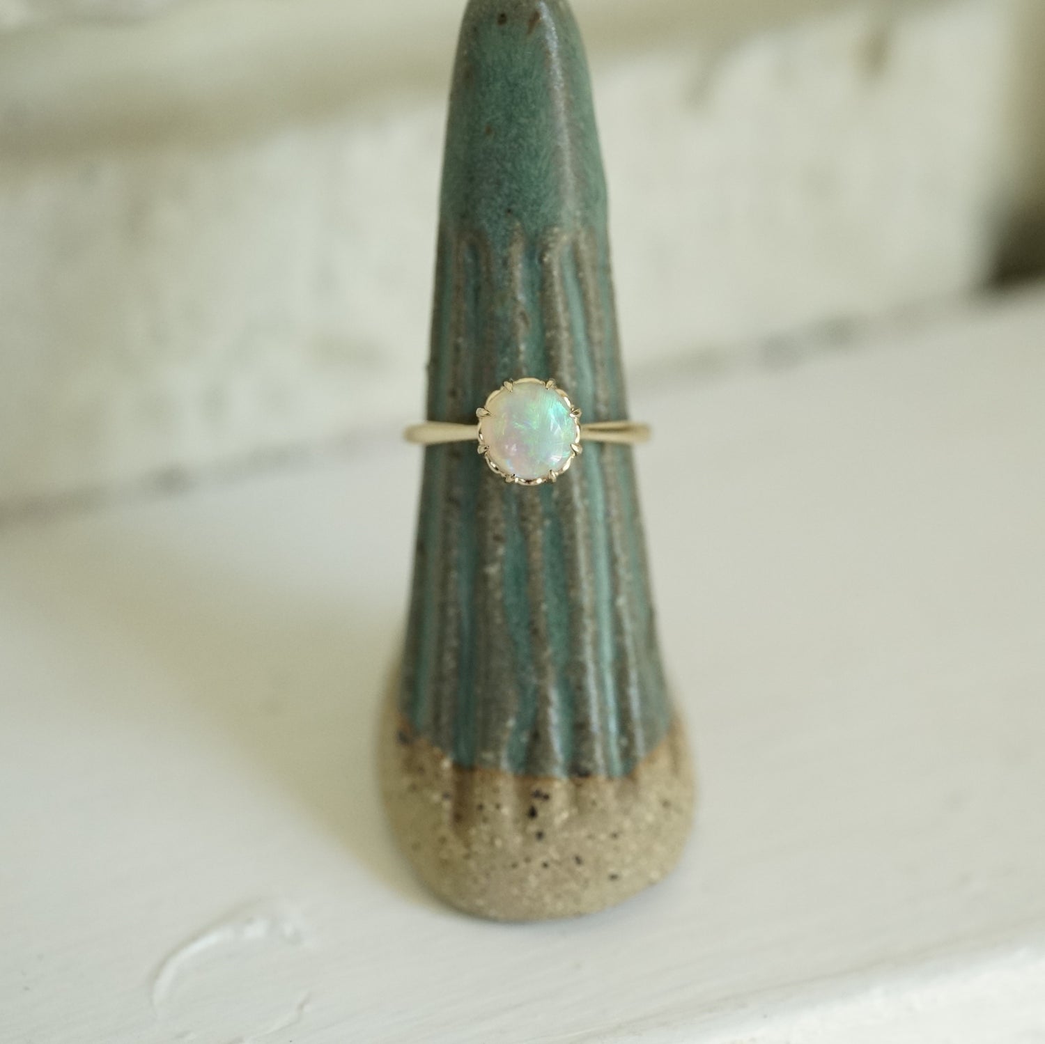 a vibrant opal with brushstroke patterns in an 8 prong yellow gold setting on a green ceramic display
