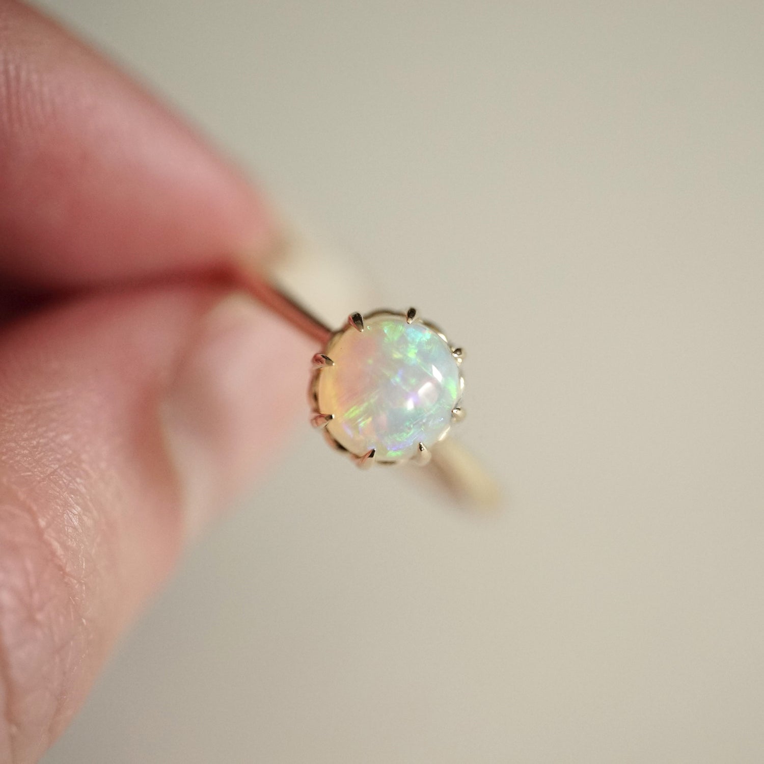 a yellow gold ring featuring a vibrant opal with brushstroke patterns held in a light skinned left hand