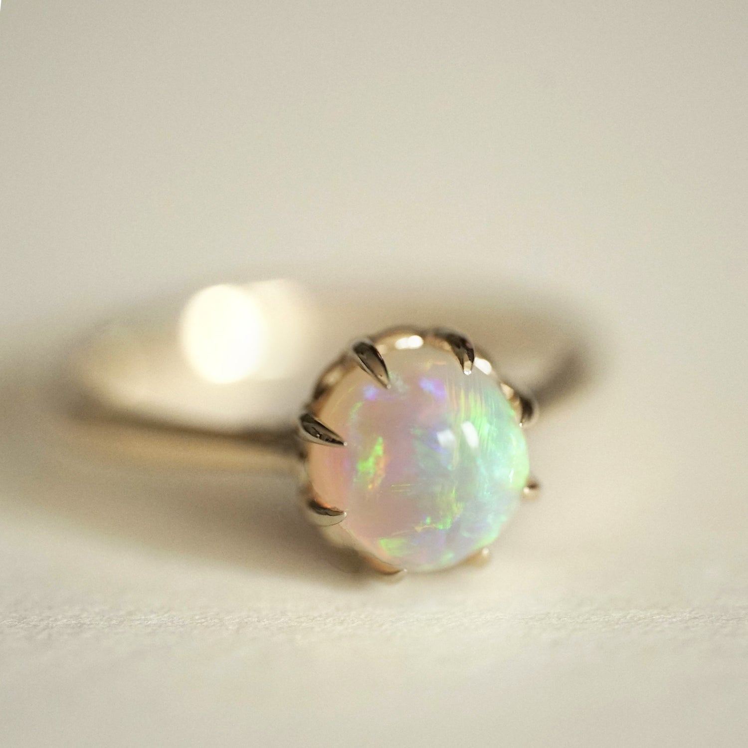 a macro photo of a vibrant opal with brushstroke patterns in an 8 prong yellow gold setting on a matte white background