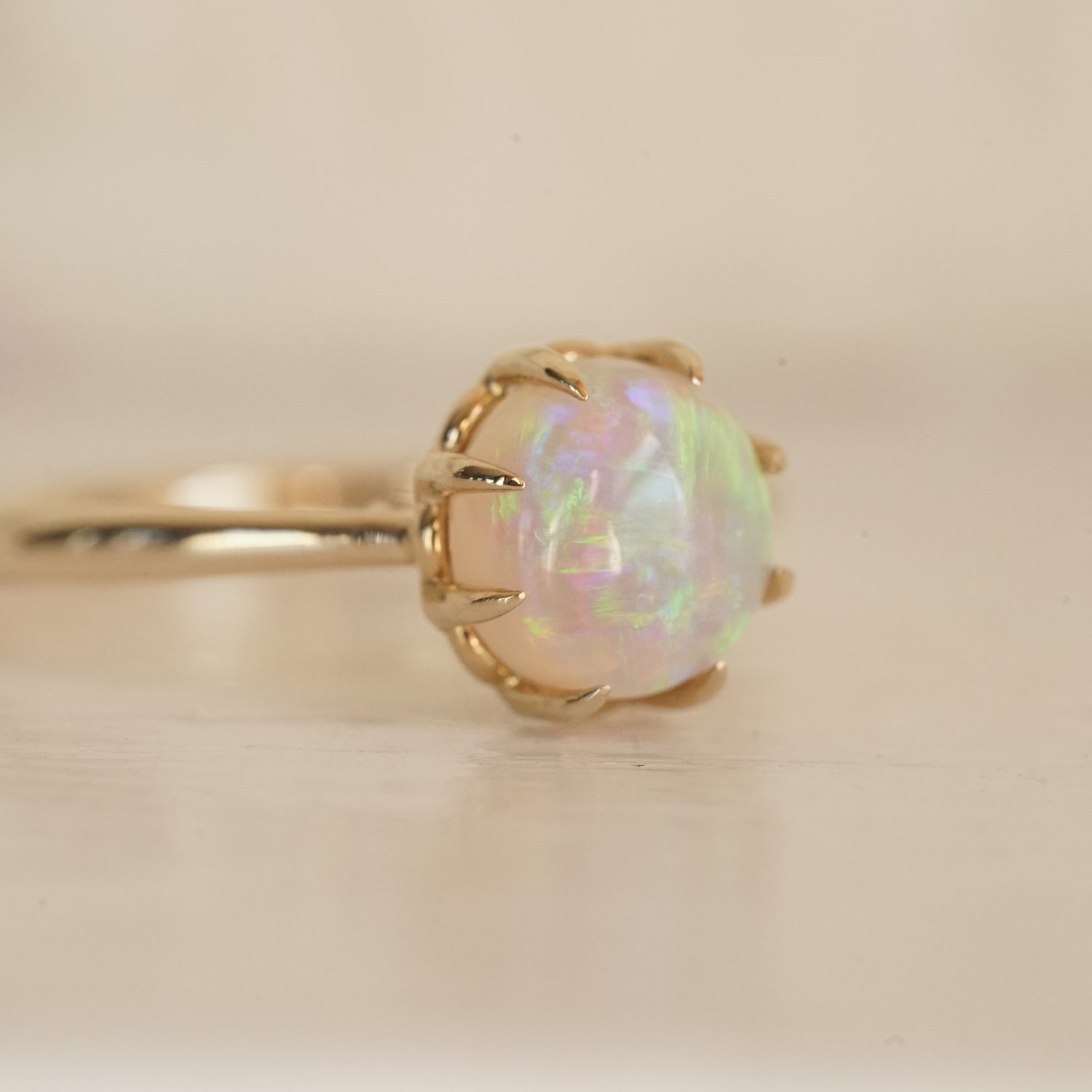 a macro photo of a vibrant opal with brushstroke patterns in an 8 prong yellow gold ring on a glossy white background