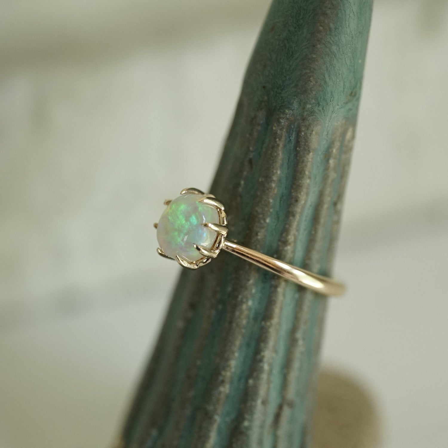 a vibrant opal with brushstroke patterns in an 8 prong yellow gold setting on a green ceramic display