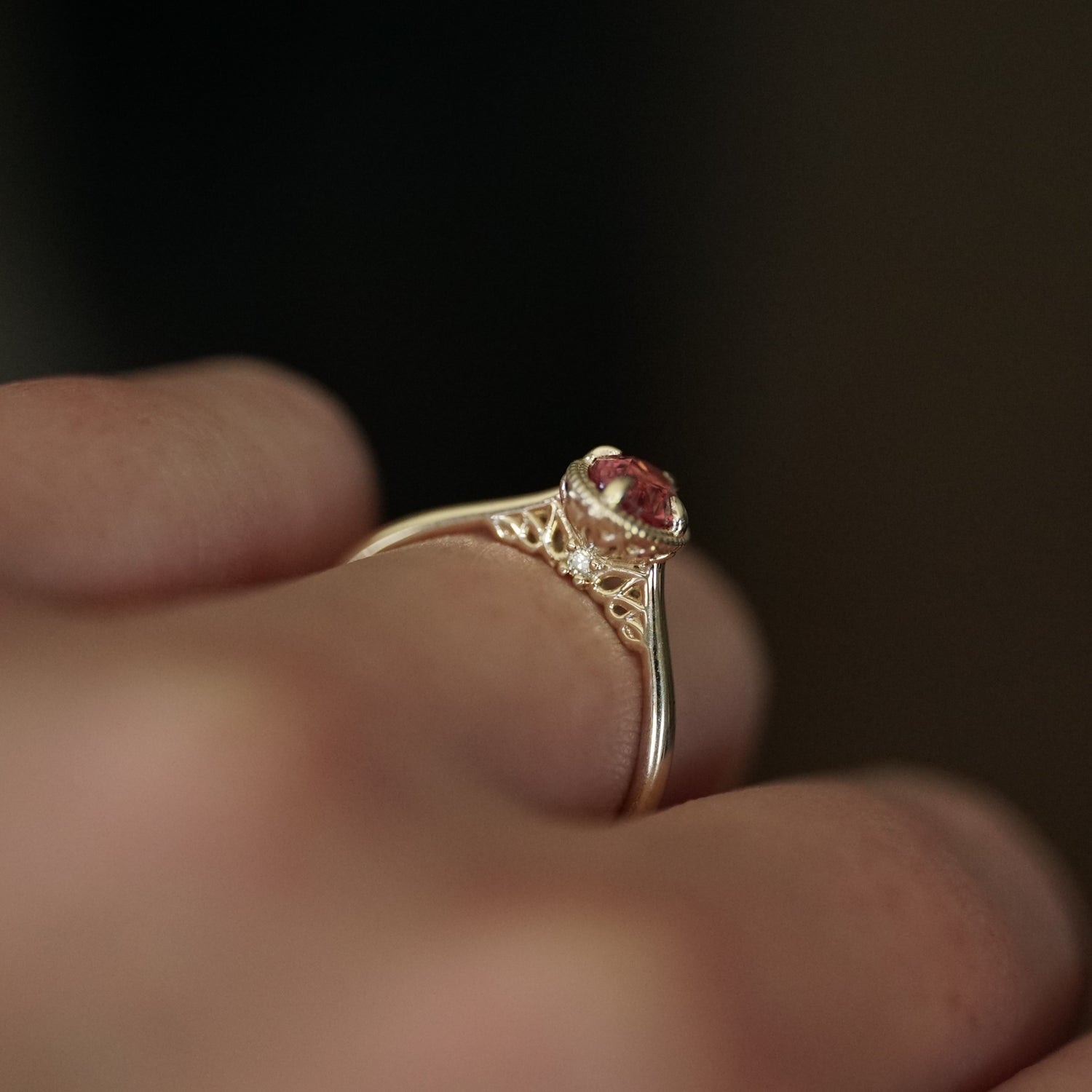 a detail shot of the side leaf design profile of a yellow gold ring with pink spinel center stone on a light skinned left hand