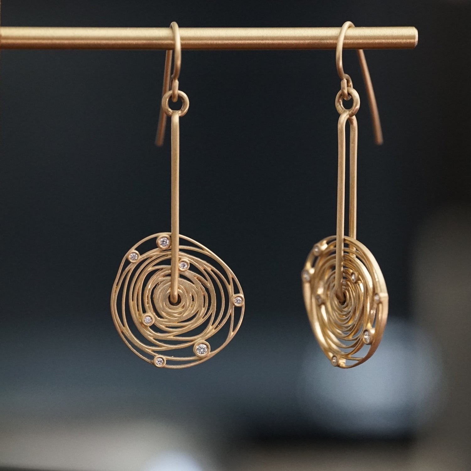 a pair of 14K yellow gold and diamond earrings with thin wirework loosely emulating the rotation of the planets around the sun hanging on a brass wire