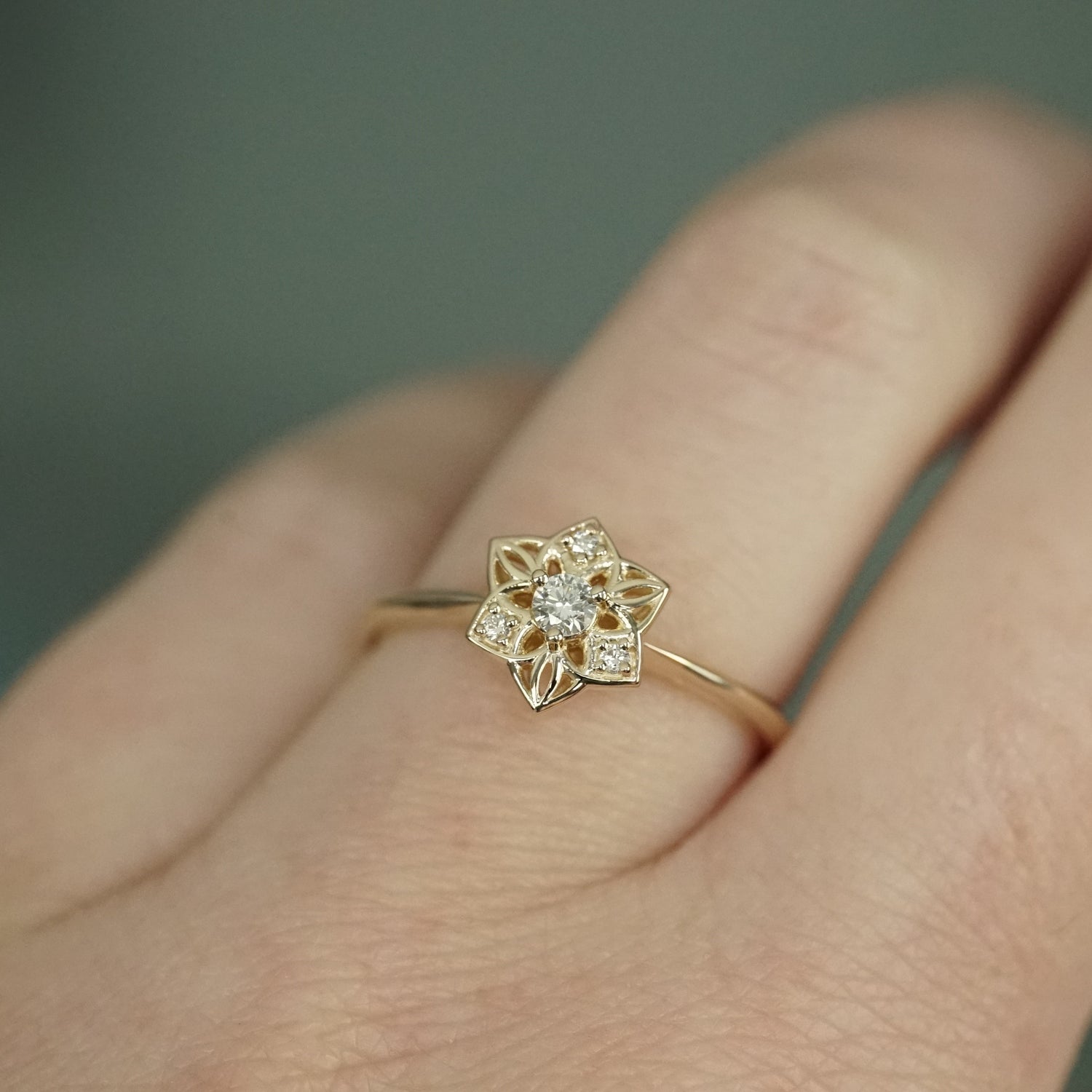 a yellow gold ring with an open wirework flower inspired by daffodils with a single diamond prong set center stone and 3 prong set accent diamonds in the petals on a light skinned left hand
