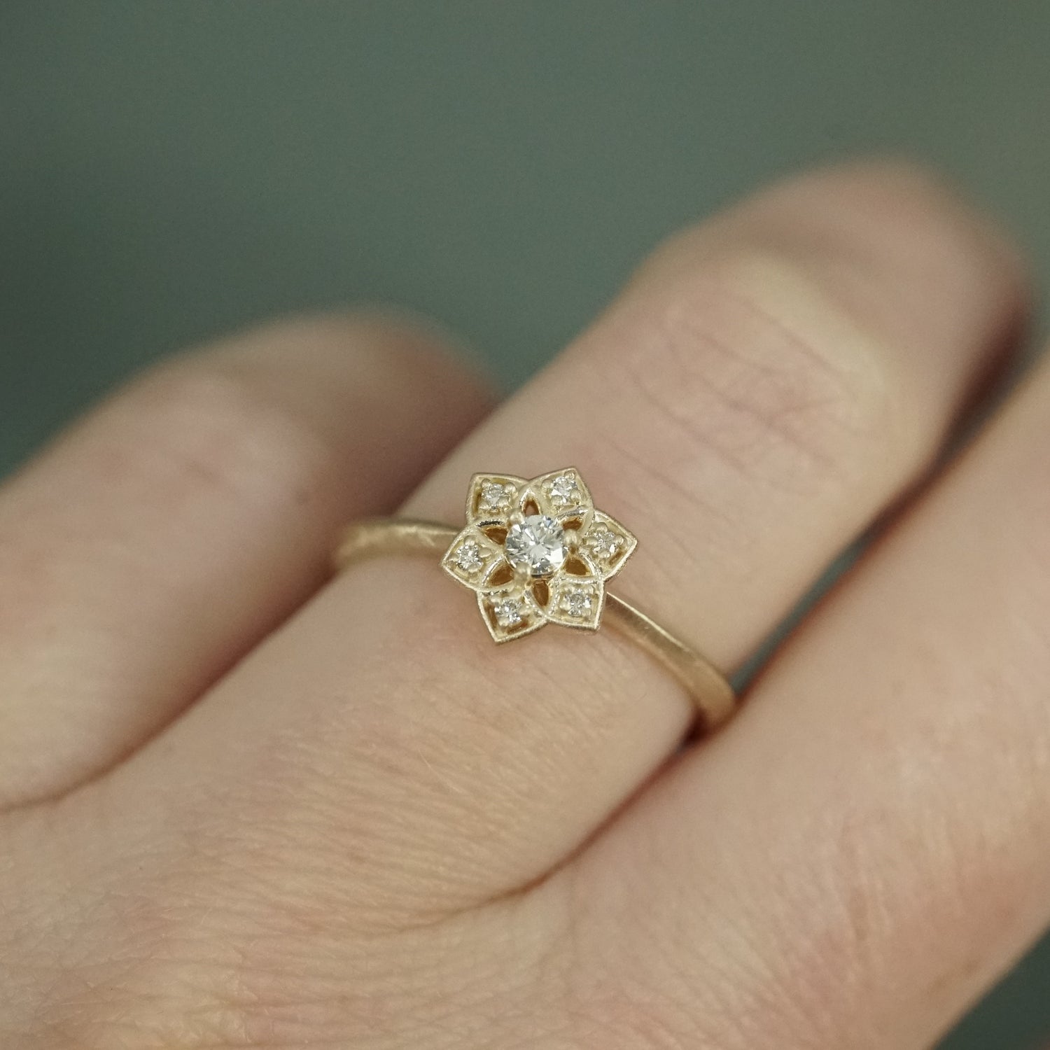a yellow gold ring with an open wirework flower inspired by daffodils with a single diamond prong set center stone and 6 prong set accent diamonds in the petals on a light skinned left hand