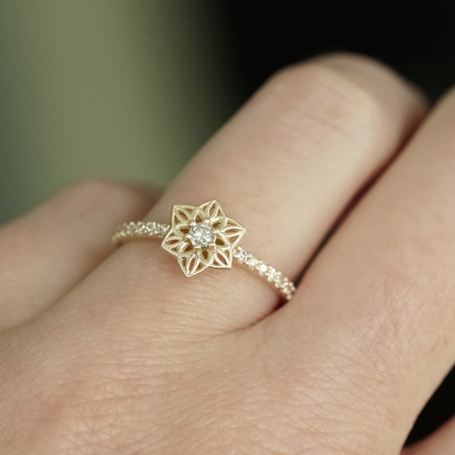 a yellow gold ring with an open wirework flower inspired by daffodils with a single diamond prong set center stone and shared prong diamonds on the shank on a light skinned left hand