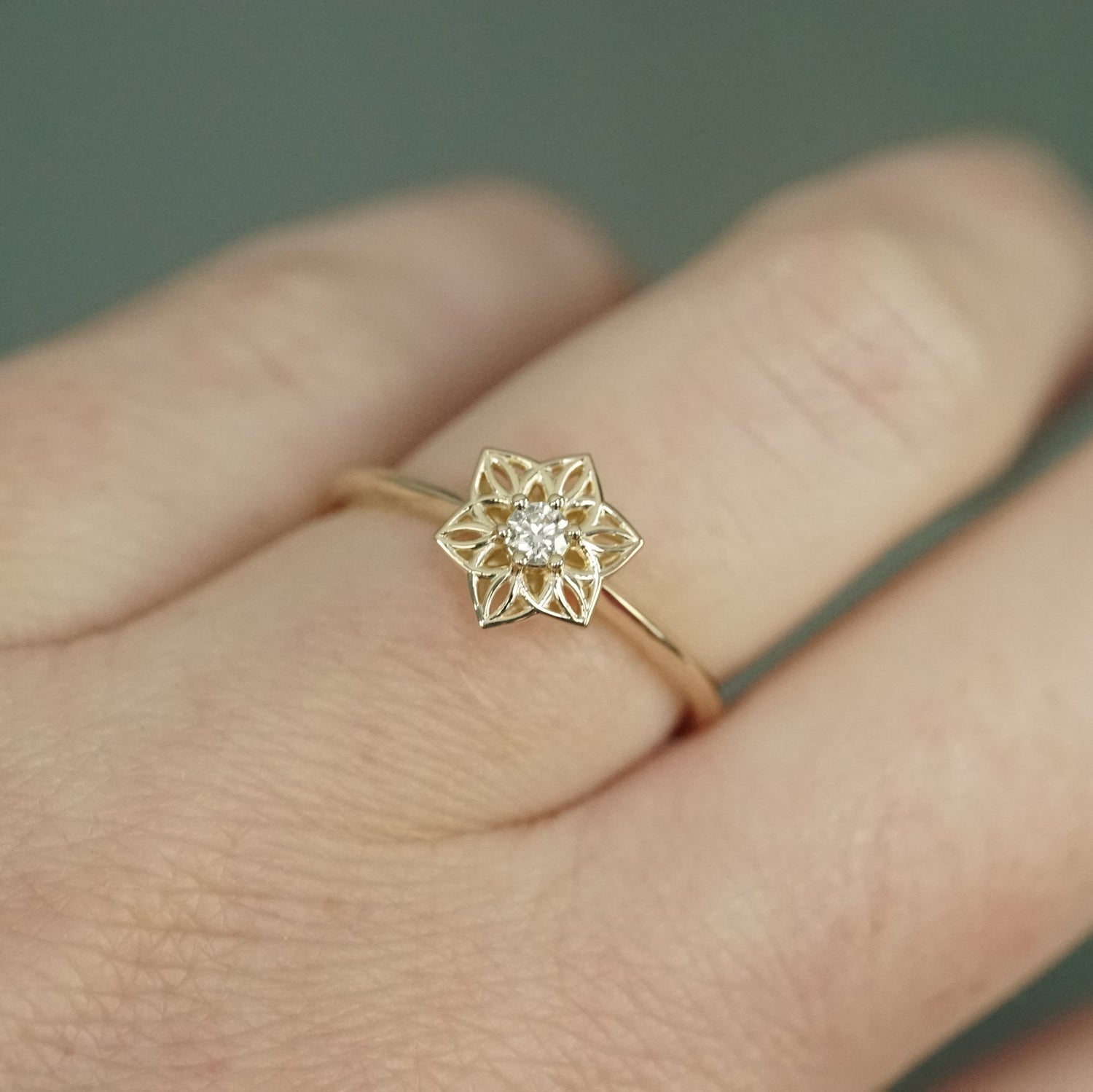 a yellow gold ring with an open wirework flower inspired by daffodils with a single diamond prong set center stone on a light skinned left hand