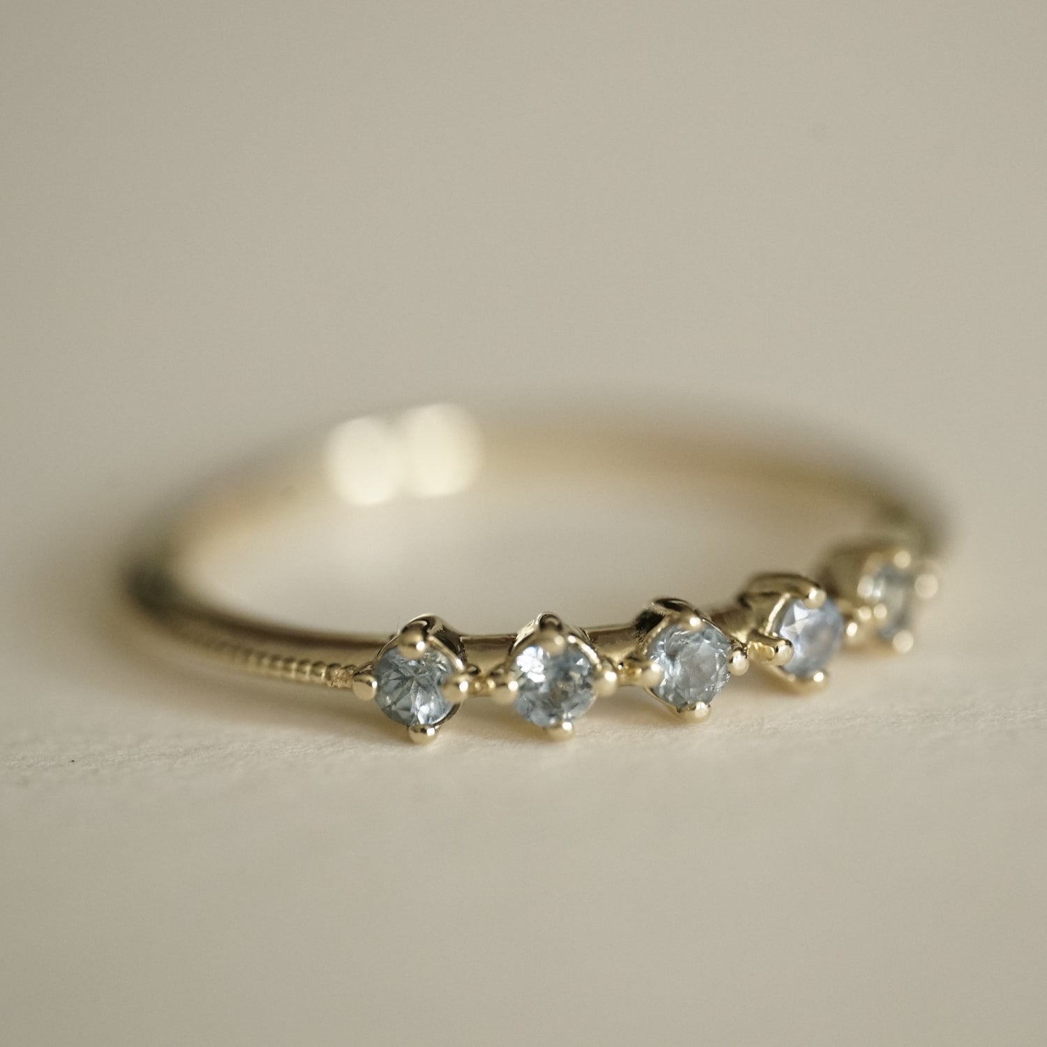 a macro photo of a ring with 5 prong set light blue sapphires on a matte white background
