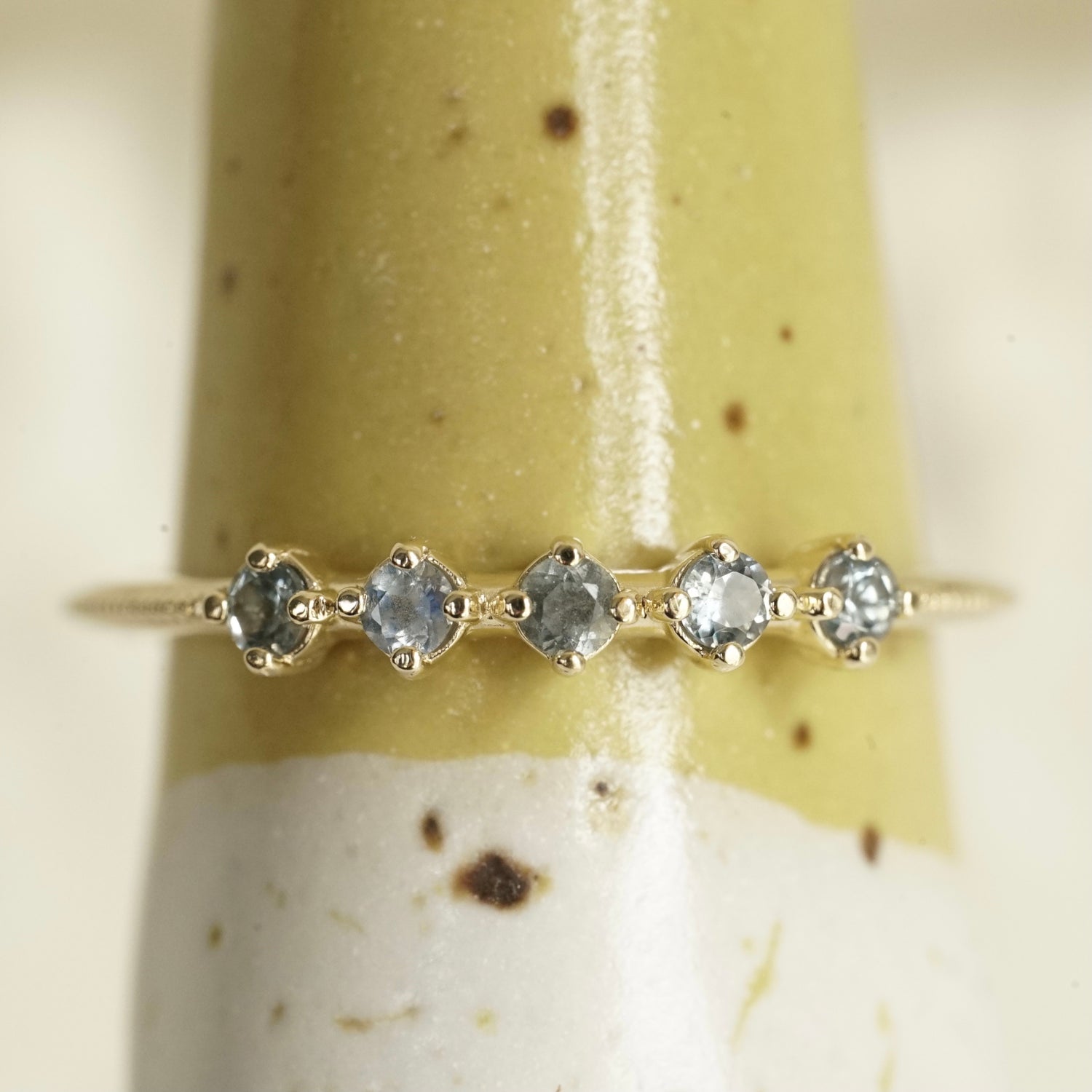 a ring with 5 prong set light blue sapphires on a yellow and white ceramic display
