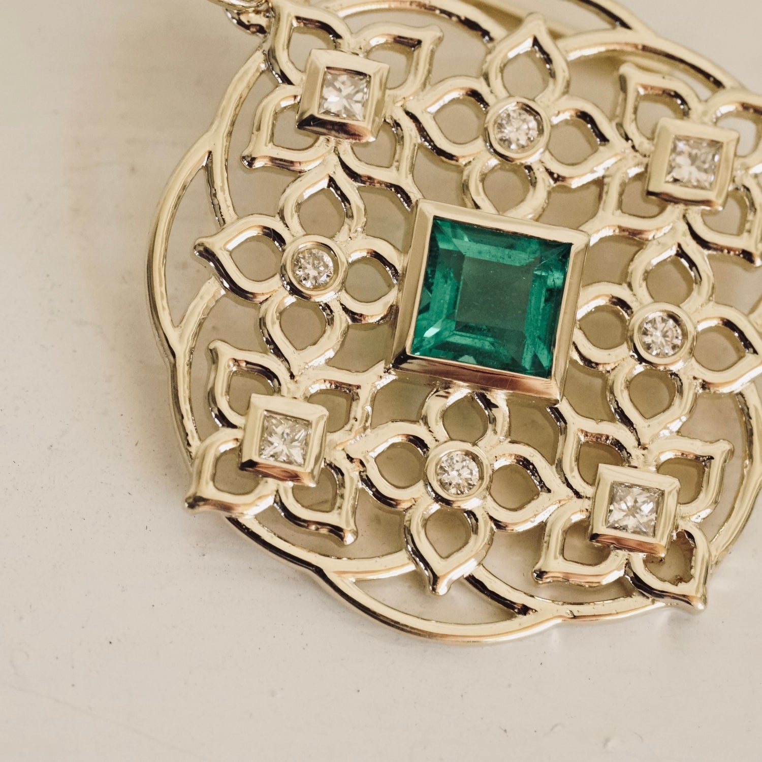 a macro photo of a yellow gold earring with princess cut emerald center stones and round and princess cut diamond earrings on a white background