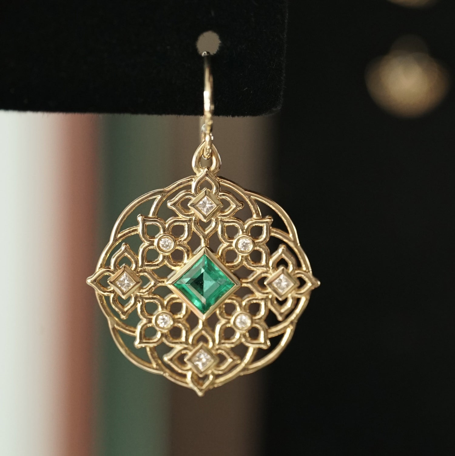 a macro photo of a yellow gold earring with princess cut emerald center stones and round and princess cut diamond earrings