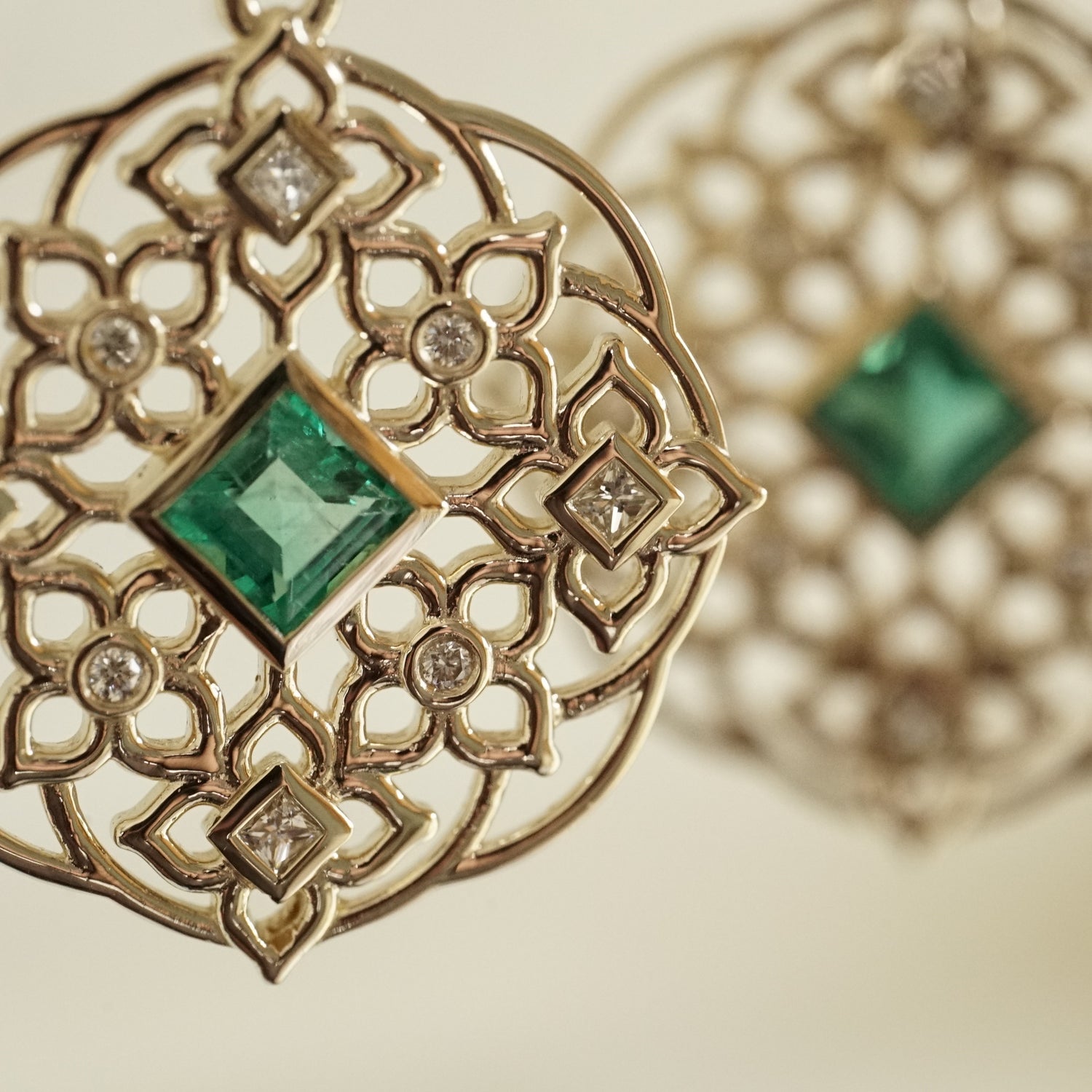 a macro photo of a yellow gold earring with princess cut emerald center stones and round and princess cut diamond earrings