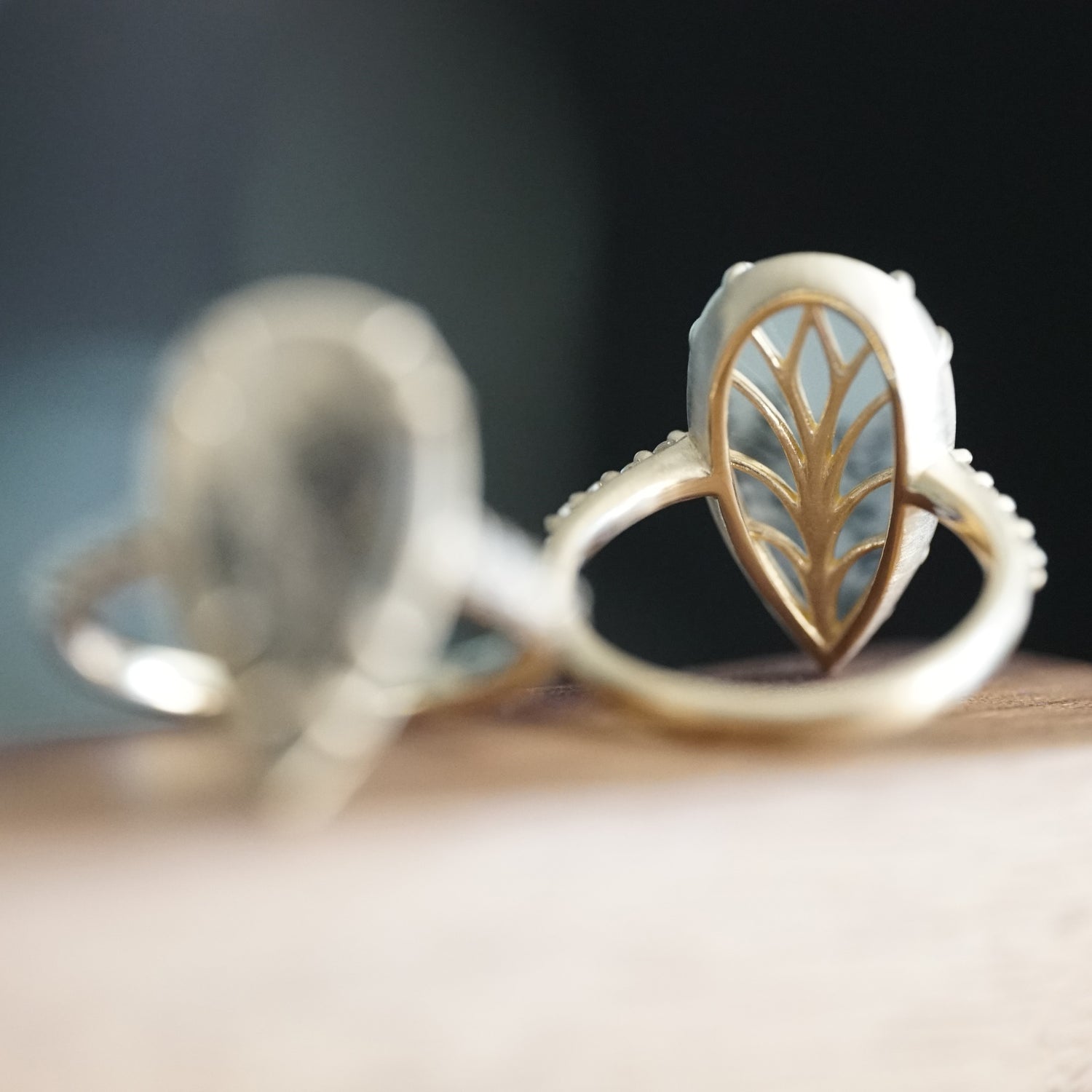 a yellow gold ring is rotated to show the backside leaf detailing and rests on a wooden base