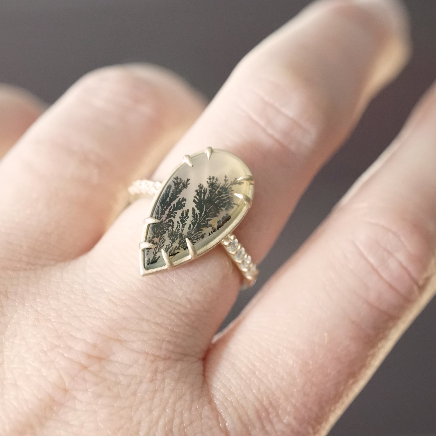 a yellow gold ring with dendritic agate center stones and diamond shanks on a light skinned left hand