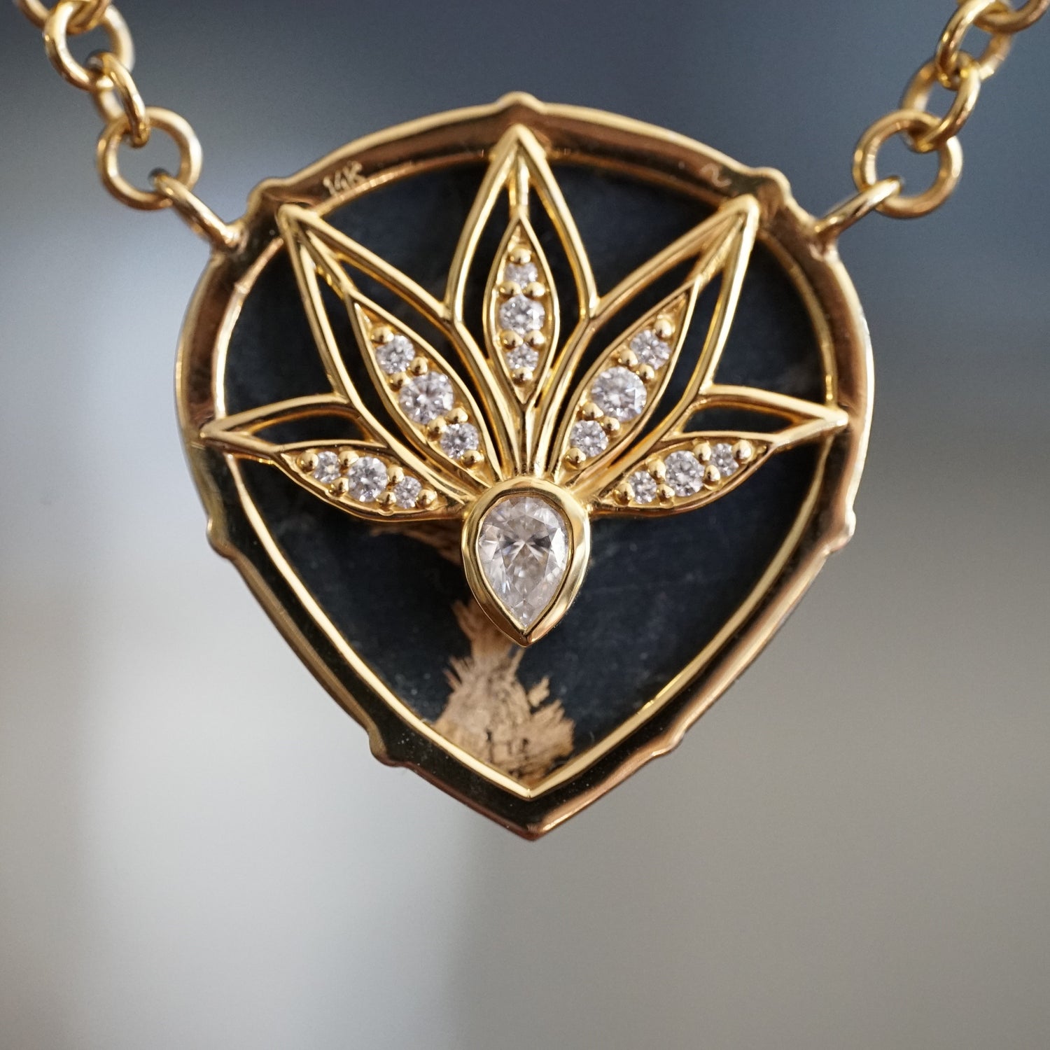 a macro photo of a yellow gold necklace featuring a pear shape black jade cabochon rotated to show the backside leaf detail design with pear shape and round white diamond accents