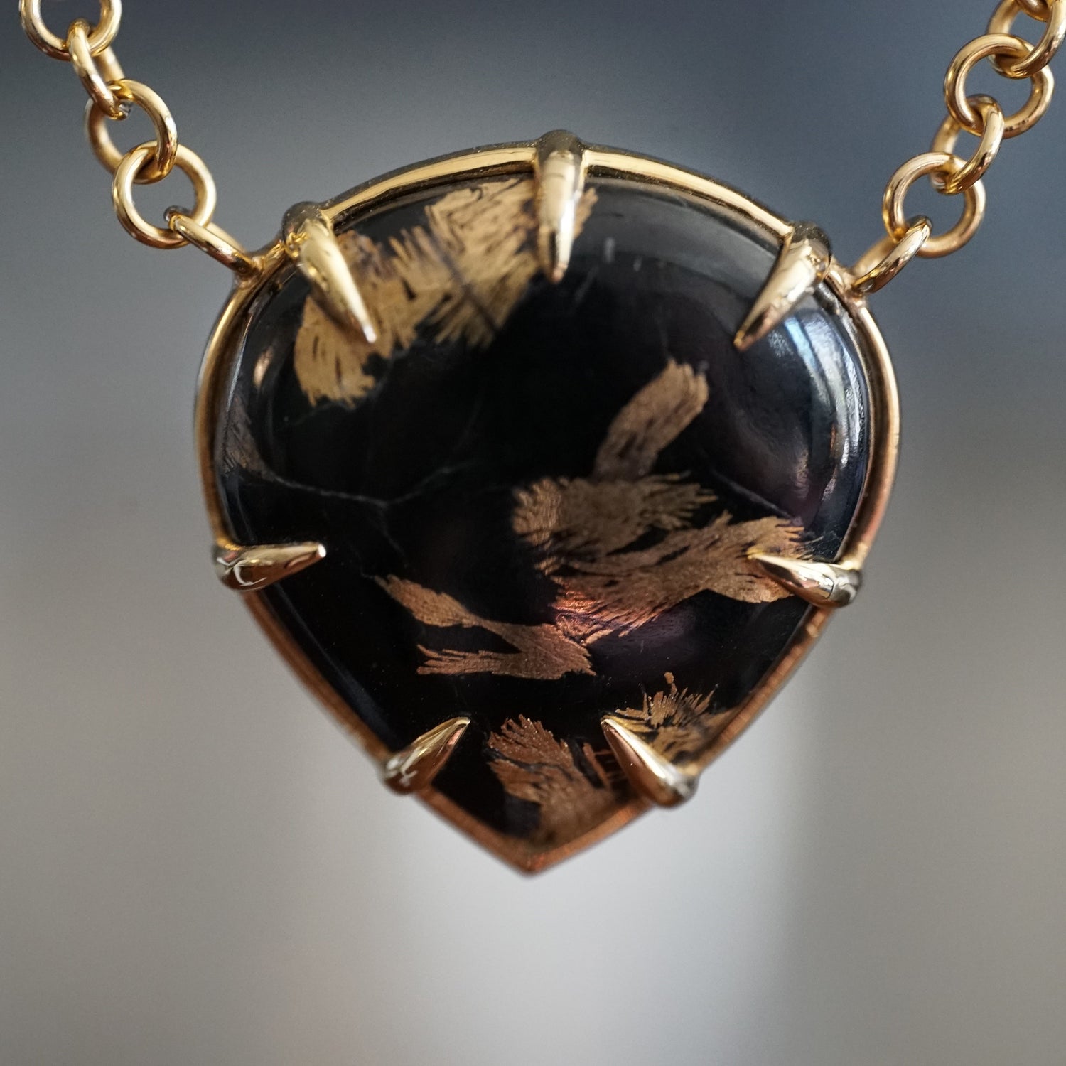 a macro photo of yellow gold necklace featuring a pear shape black jade cabochon focused on highlighting the 24K gold plating on the stones natural inclusions