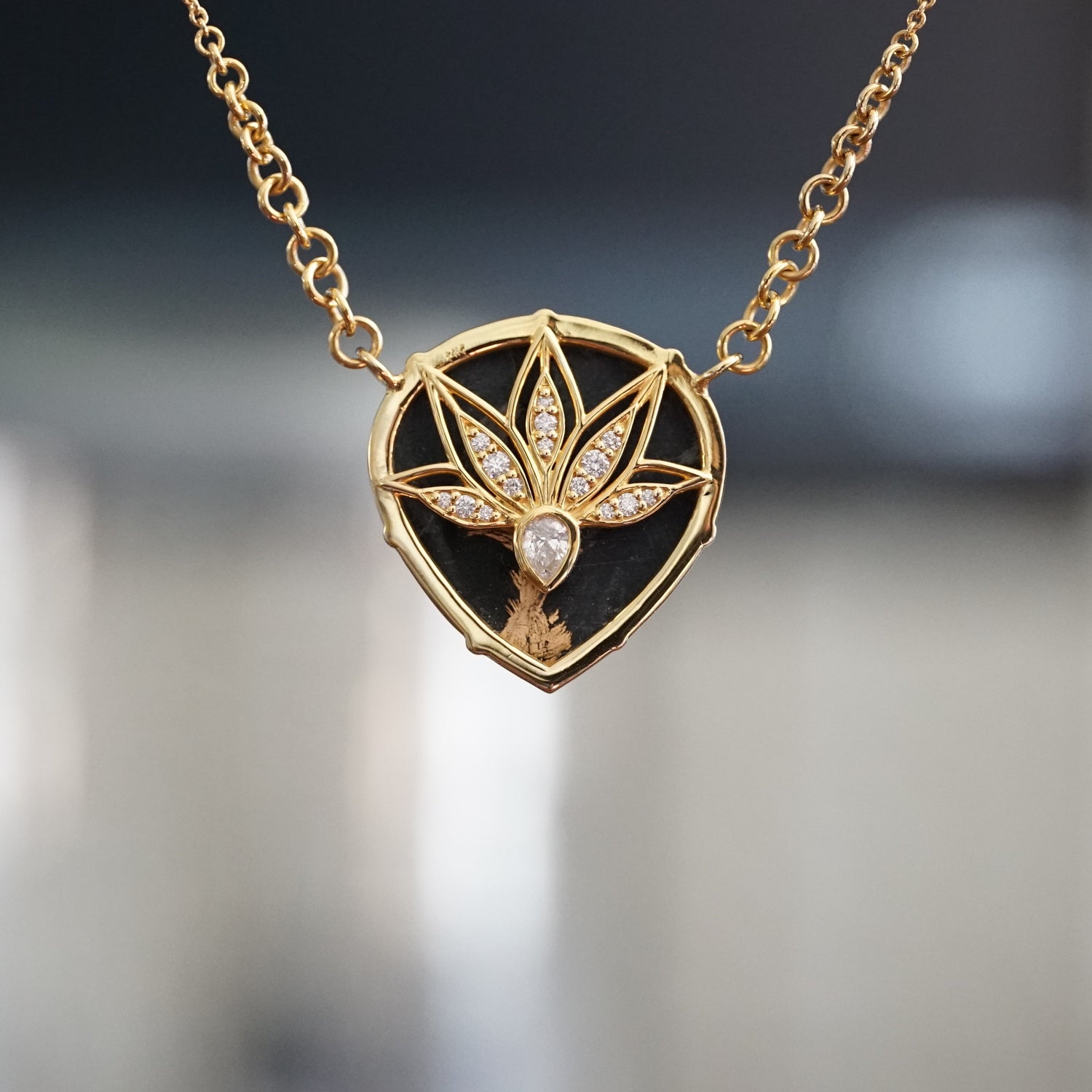 a yellow gold necklace featuring a pear shape black jade cabochon rotated to show the backside leaf detail design with pear shape and round white diamond accents