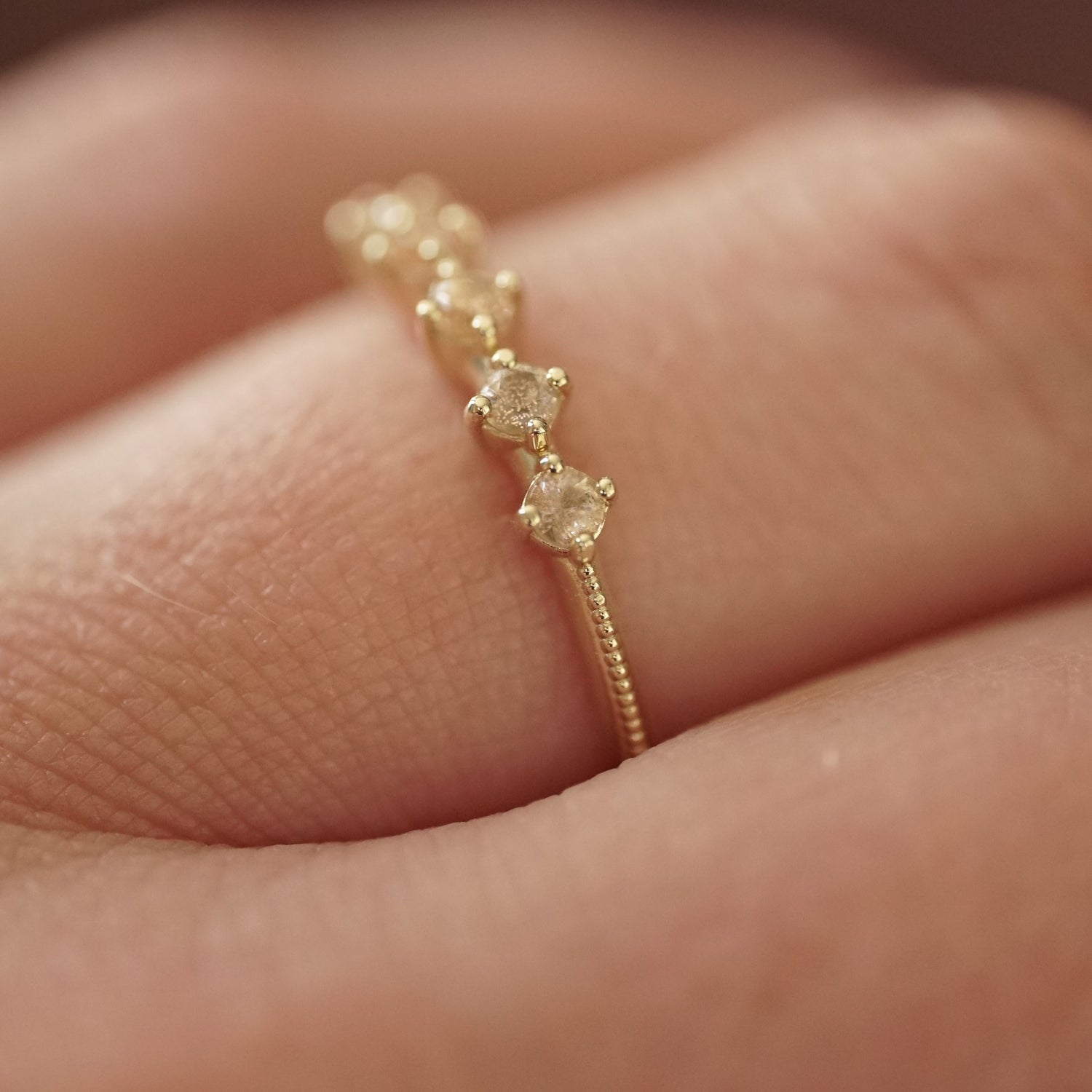 a macro photo of a yellow gold ring with 5 round light pink Oregon sunstones and migraine detail on the shank on a light skinned left hand