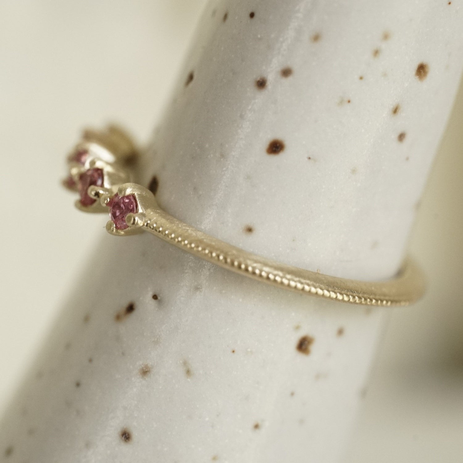 a yellow gold band with 5 prong set pink padparadscha sapphires and migraine detail on the band on a white ceramic display