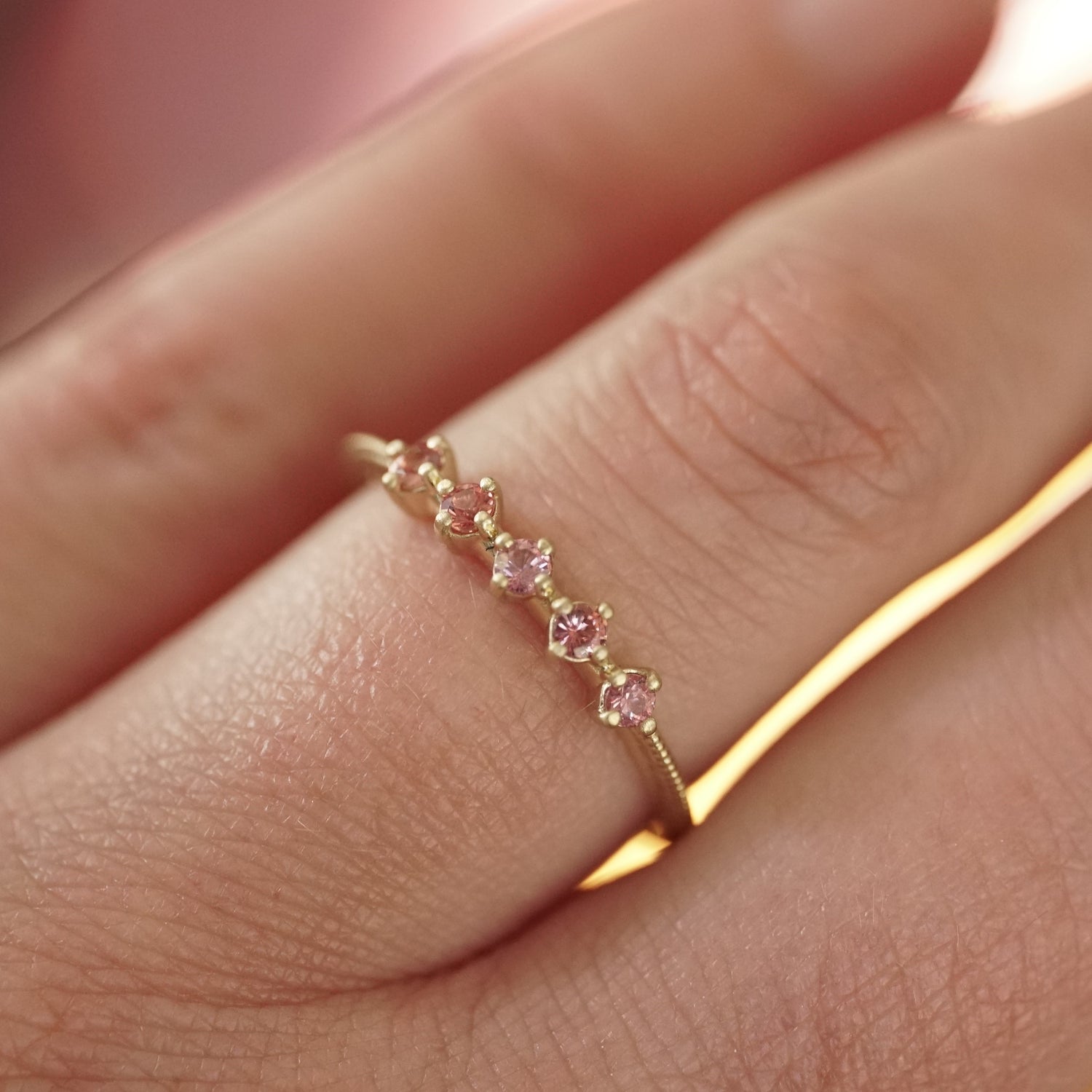a yellow gold band with 5 prong set pink padparadscha sapphires on a light skinned left hand