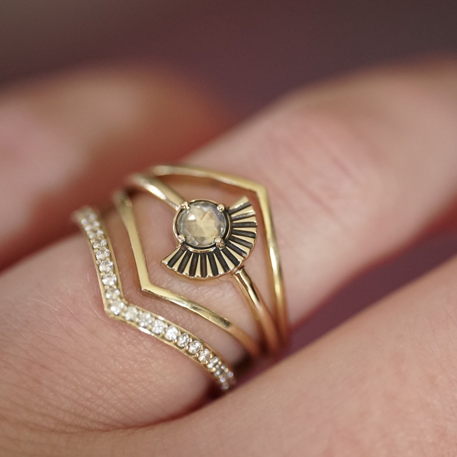 a rose cut white diamond ring with deco fan element to one side is stacked with v shape shadow bands, one with diamonds and 2 without on a light-skinned left hand