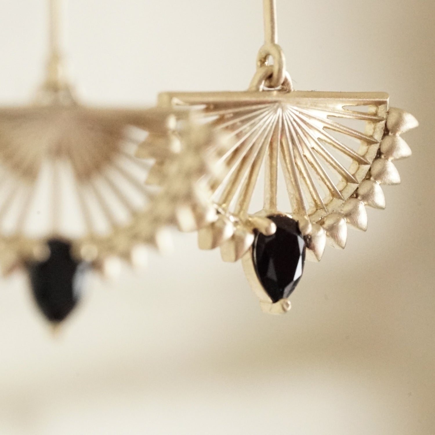 A macro photo of a pair of deco inspired matte finish yellow gold drop earrings with pear shape black onyx on a white background