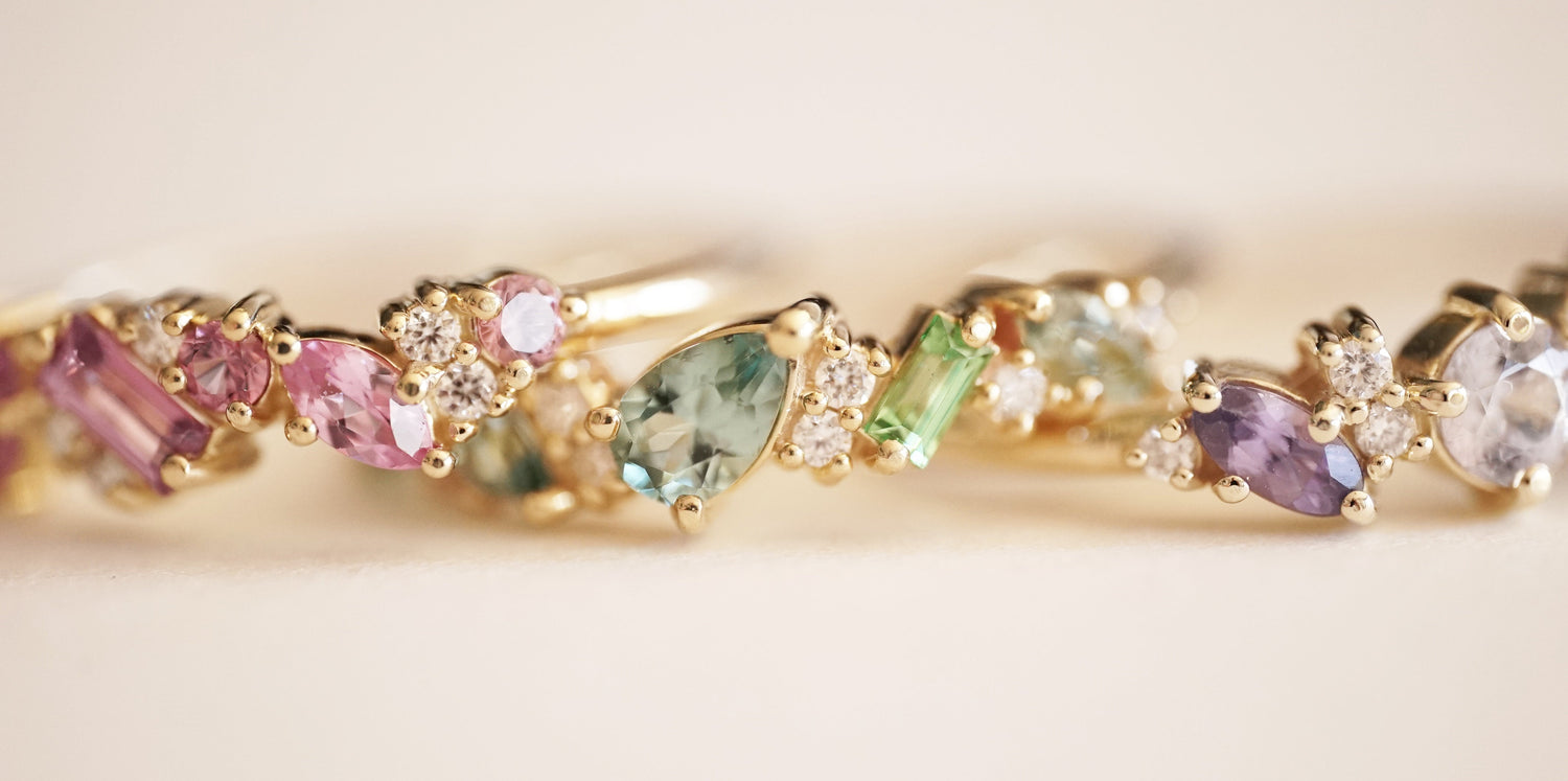 3 multi color gemstone and diamond yellow gold rings stacked in a line on a tan background