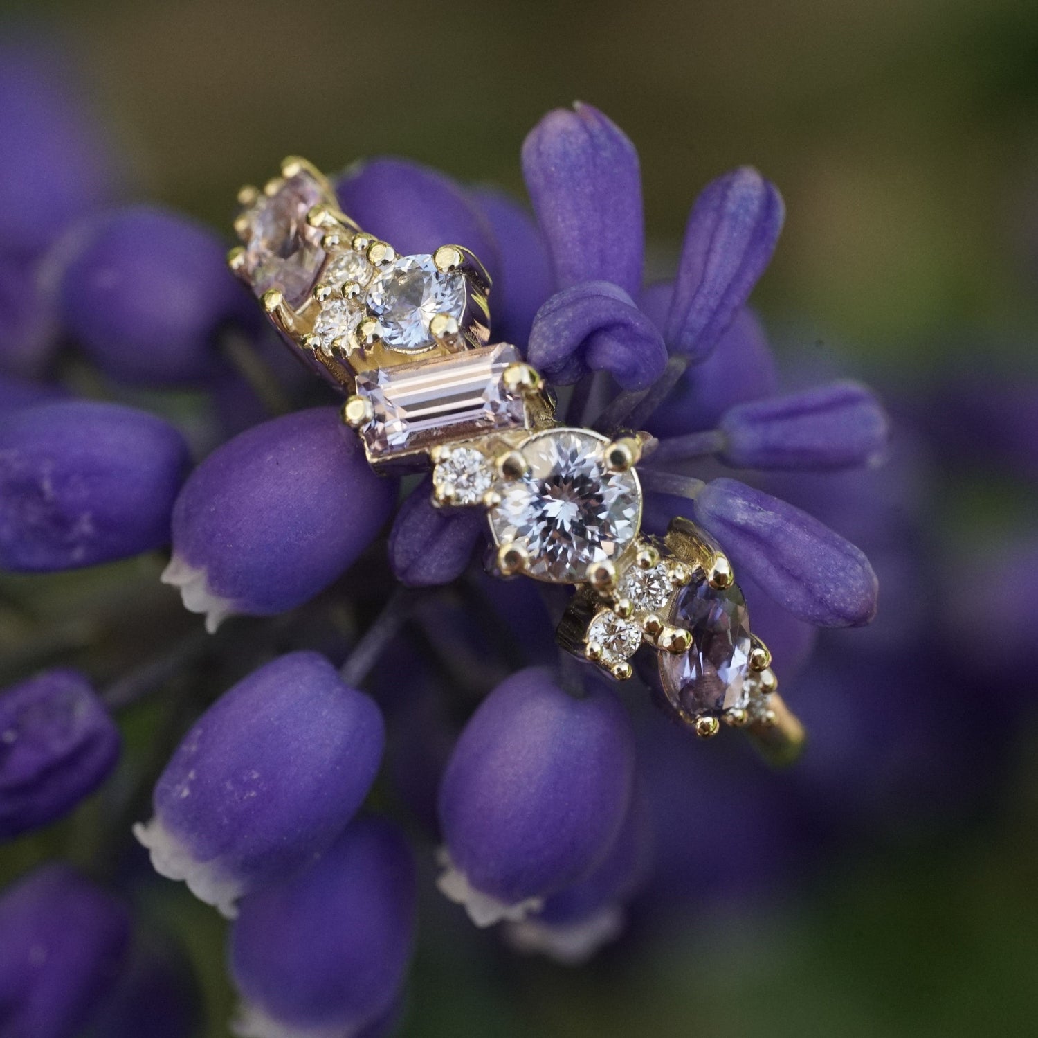 a yellow gold ring with blue and purple gems are accented with white diamonds and shown on a purple flower