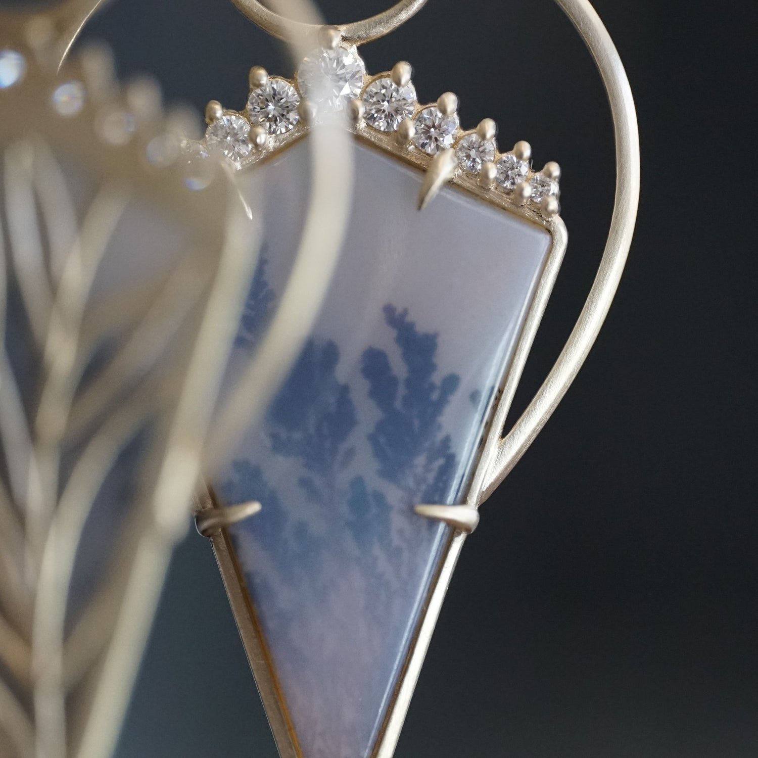 A macro photo of a yellow gold, dendritic agate, and diamond drop earring with a unique kite shape profile