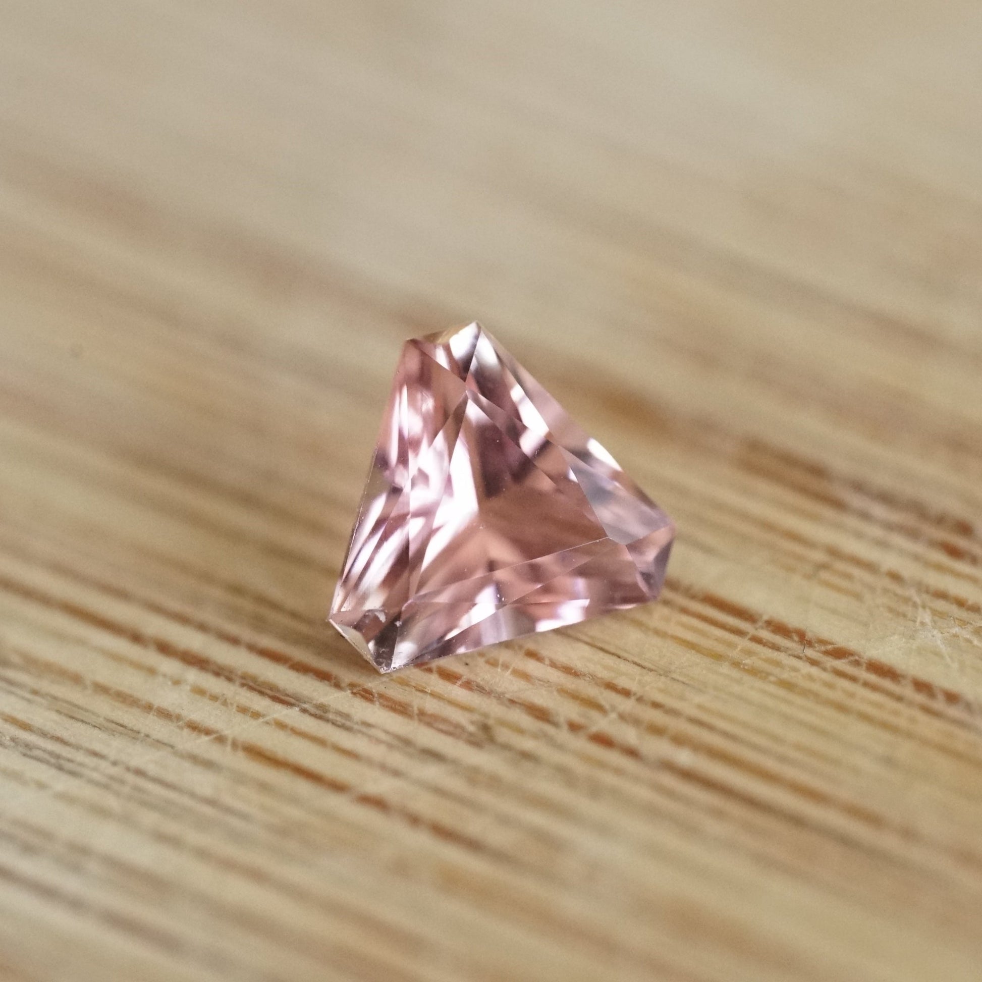 a 0.85 ct pink tourmaline trillion rests on a wood base