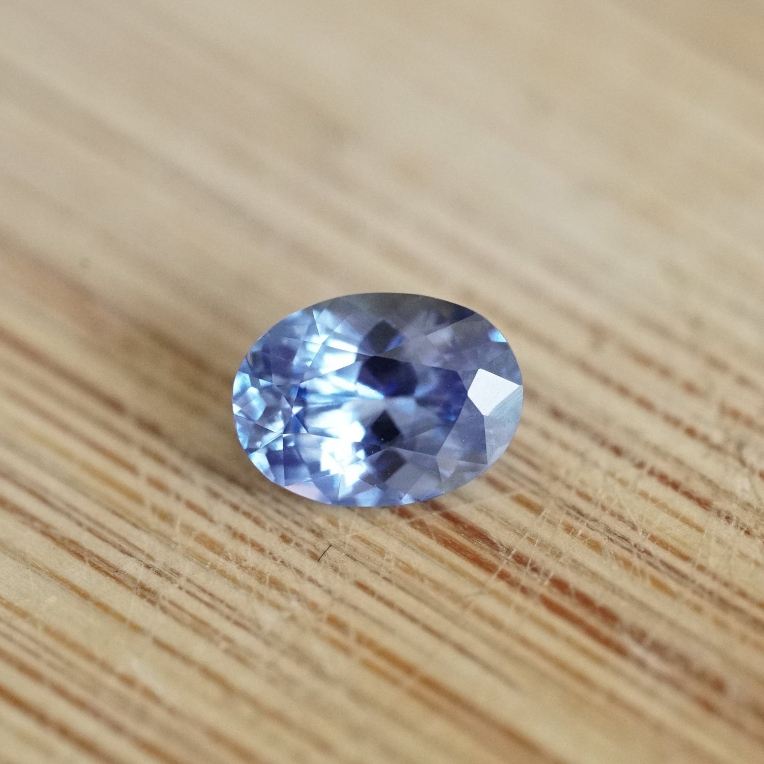 a 1.06 ct oval periwinkle blue sapphire rests on a wood base