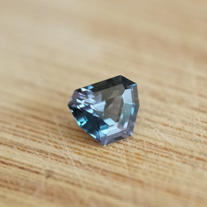 a 1.11 ct teal spinel shield shape gem on a wood base