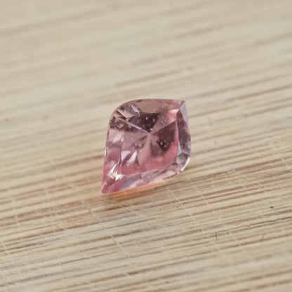 a 1.31 ct slightly organey pink sapphire in a rounded kite shape on a wood base