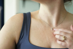 A close-up lifestyle shot of a woman wearing a delicate silver chain necklace with a small pendant, paired with a navy blue tank top.