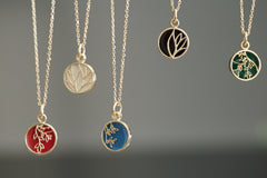 10K Yellow Gold and Cold Enamel Pendants are suspended in front of a grey background