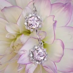 a pair of white gold earrings with a synthetic yag center stone and diamond accents rests on a pink and yellow flower