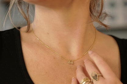 a yellow gold necklace with two small carved pendants shown on a light skinned model