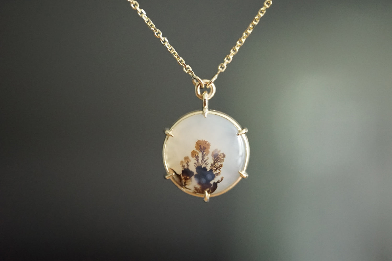 Gold necklace with a round pendant featuring dried flowers on a dark background