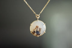 Gold necklace with a round pendant featuring dried flowers on a dark background