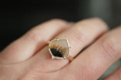 Close-up of a hand wearing a gold ring with a black and brown stone.