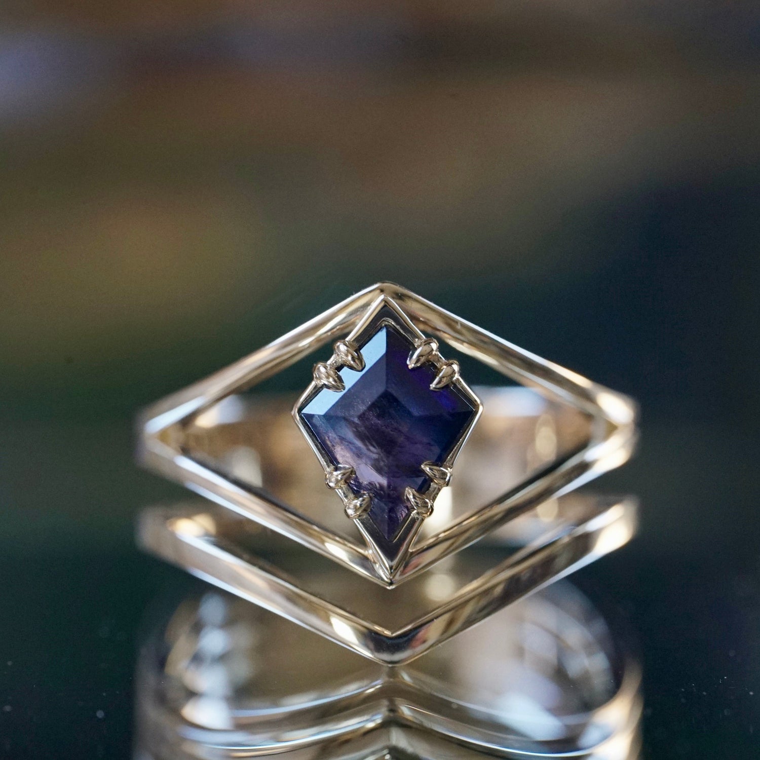 A close-up of a yellow gold ring with a solitaire sapphire centerpiece, displayed on a reflective surface.