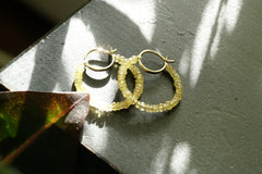 Gold hoop earrings on a textured surface with a leaf shadow.