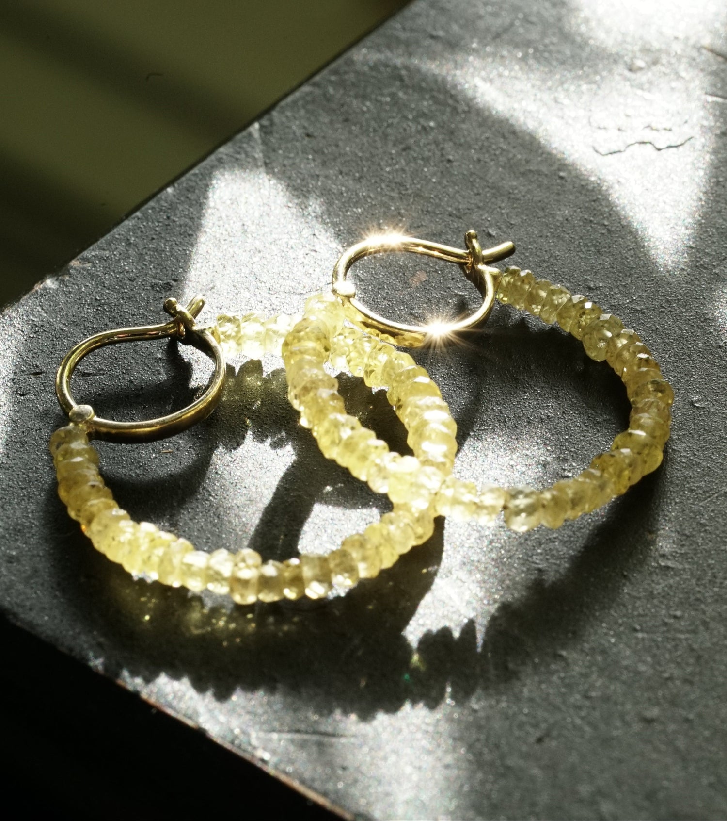 Gold hoop earrings on a textured surface with sunlight casting shadows