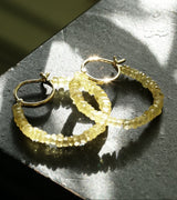 Gold hoop earrings on a textured surface with sunlight casting shadows