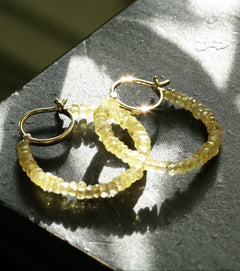 Gold hoop earrings on a textured surface with sunlight casting shadows