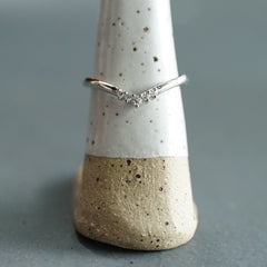 A white gold and diamond V shaped shadow style wedding band on a white ceramic display with a blue grey background