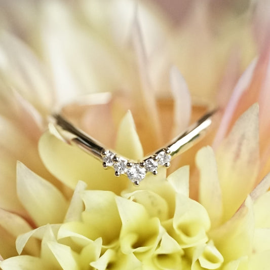 A white gold and diamond V shaped shadow wedding band laying on a pink and yellow flower